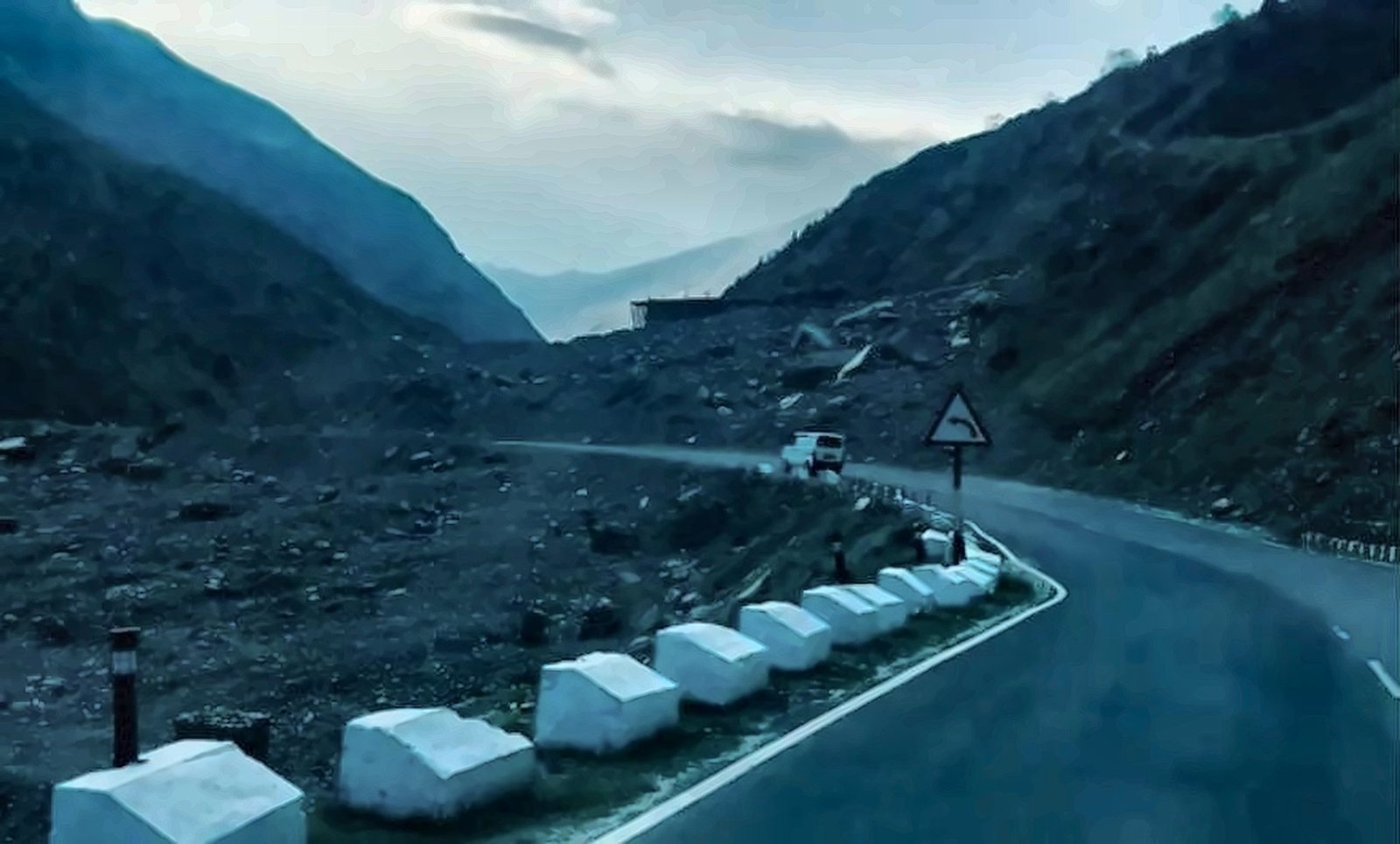 White roadside stones along a quiet hill road at blue hour